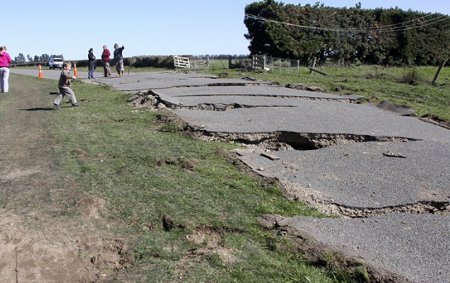 A group of adults inspect an earthquake cracked road while children play near it