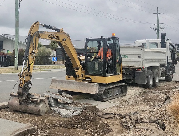 A digger digging a footpath with a truck behind