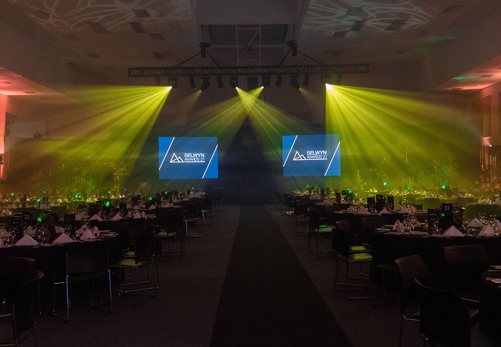 A yellow and red light show across a series of laid tables with screens at the end say Selwyn Awards