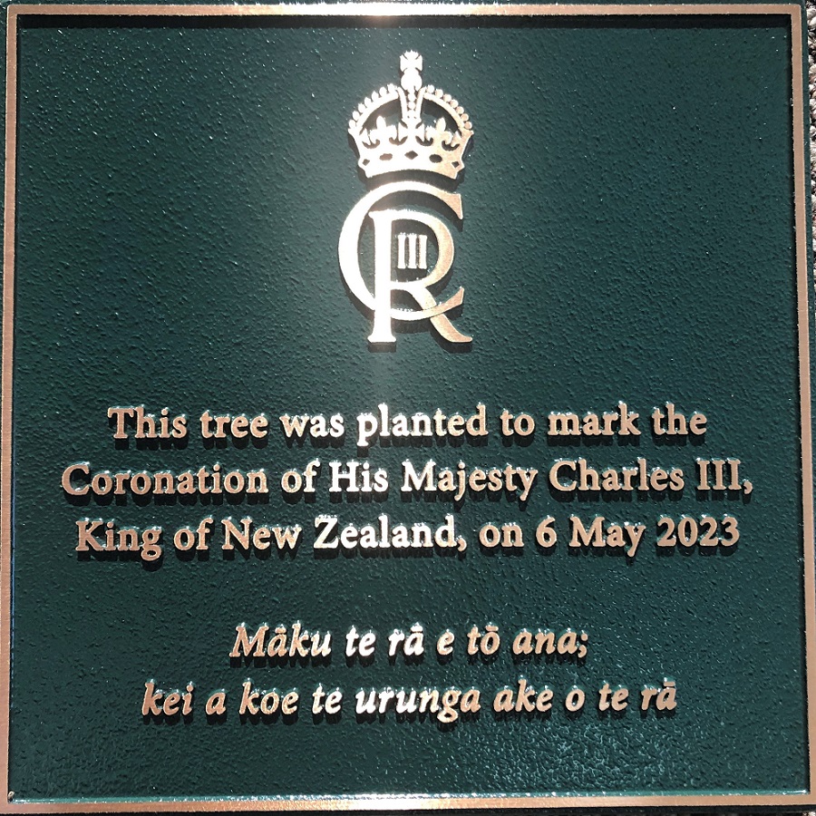 close up image of green plaque with brass lettering noting 'This tree was planted to mark the Coronation of His Majesty Charles III, King of New Zealand, on 6 May 2023 Māku te rā e tō ana; kei a koe te urunga ake o te rā