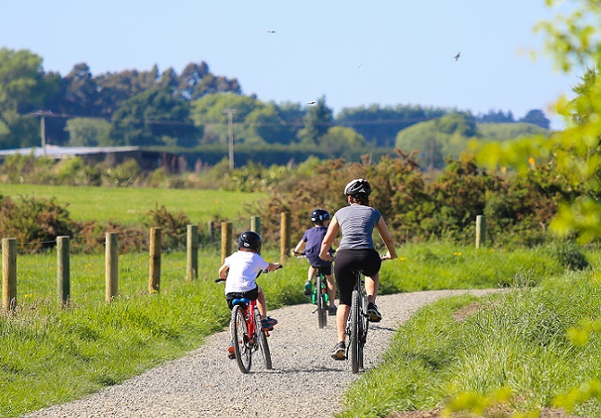 Mum and two children riding a bike trail through some fields