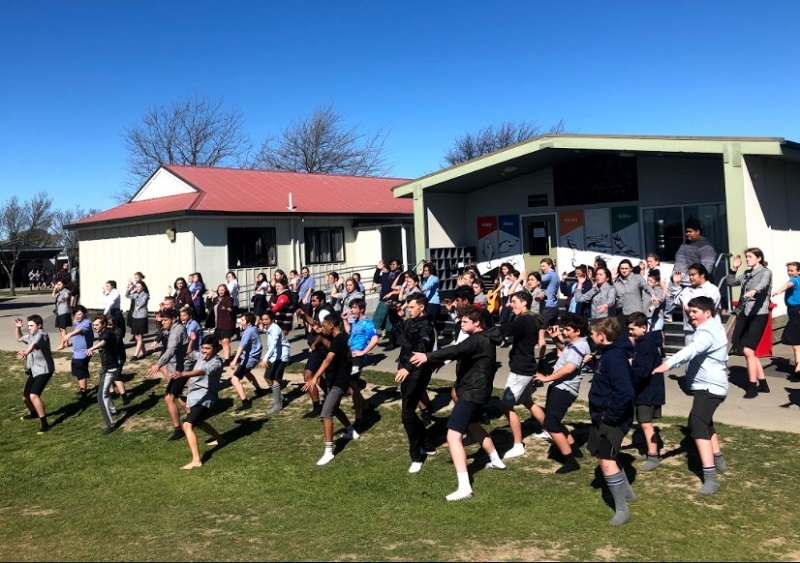 A group of students performing kapa haka in front of a school classroom
