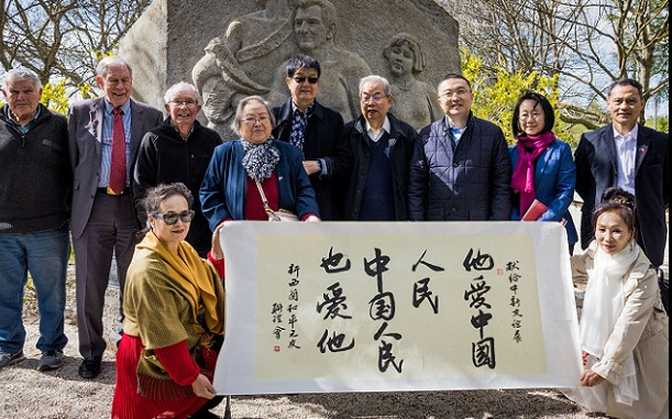 A line of people standing in front of the Rewi Alley memorial, with two women in traditional Chinese dress in front holding a sign written in Mandarin