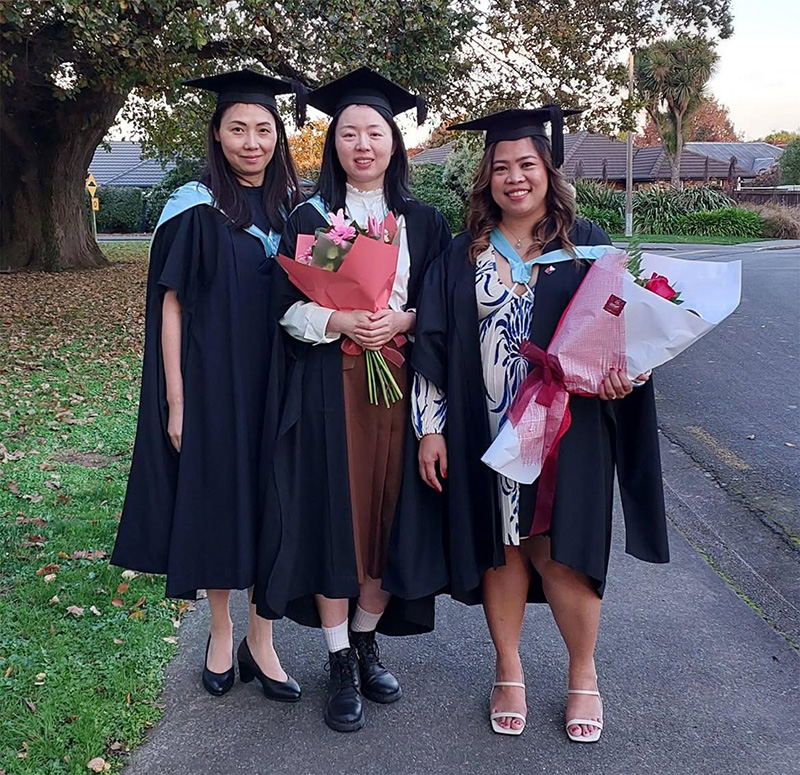 Three women graduates stand with flowers in hands