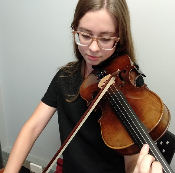 Close up of teenage girl with brown hair and glasses playing the violin