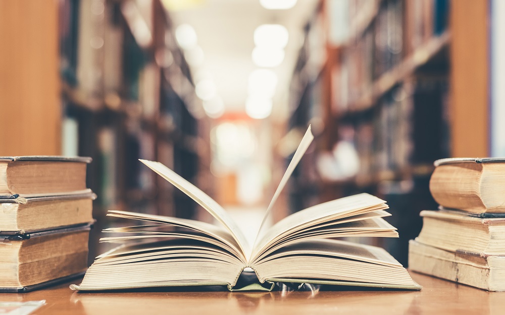 An open book sitting on a desk in a library with closed books either side
