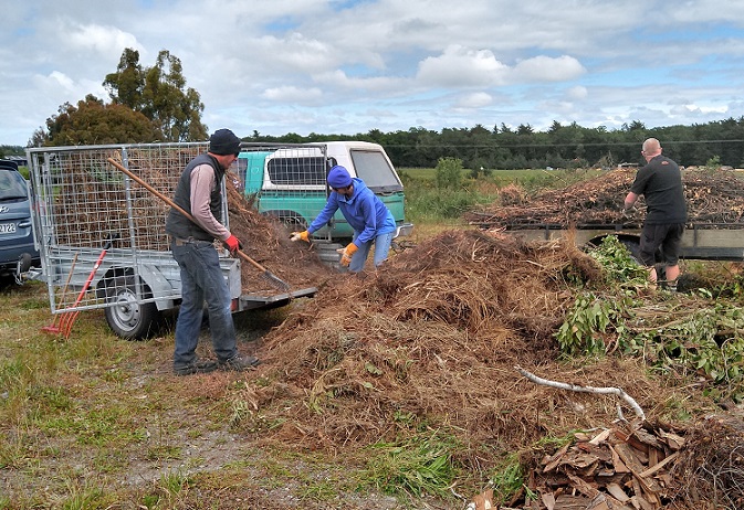 Three people unloading trailers of green waste into a pile