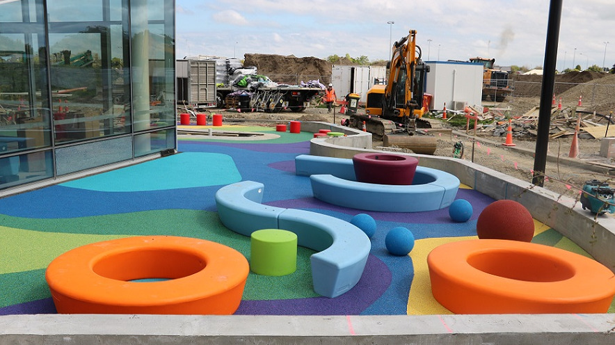 colourful soft fall, curved seats and balls inside a concrete walled area with a building site around
