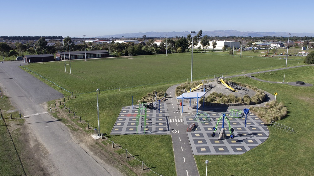 aerial image of sports fields and a playground with soft fall in squares, and a low hill with a slide on it