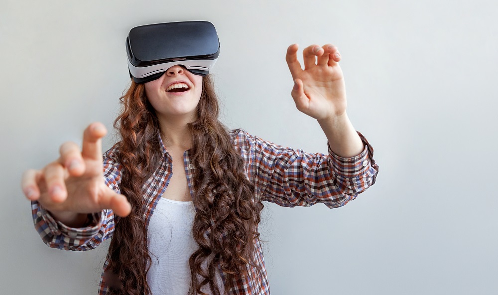 Brown haired woman in check shirt has hands outstretched while using a virtual reality headset
