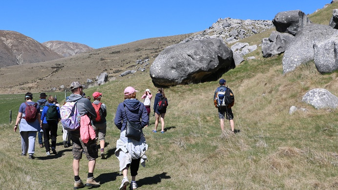 A group of walkers walk to the right of boulders at Castle Hill