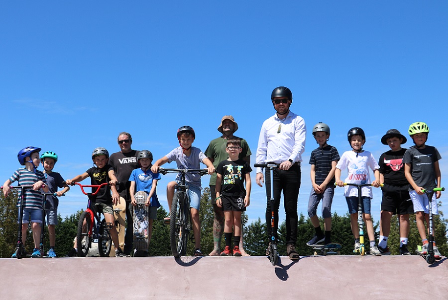 A line of of children and Mayor Sam Broughton on a range of skateboards, scooters and bikes at the top of a ramp