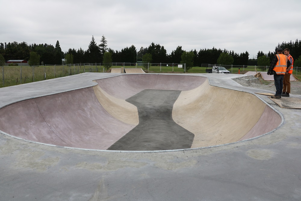 Two people in high vis vests talk inspect a skate park bowl