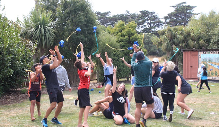 A crowd of young people on a lawn throwing poi in the air