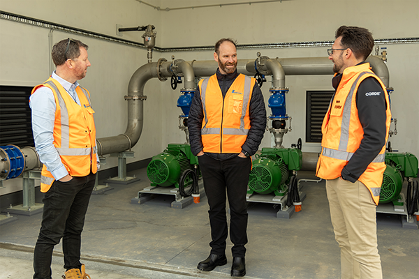 Three men stand in the pumpstation talking to each other