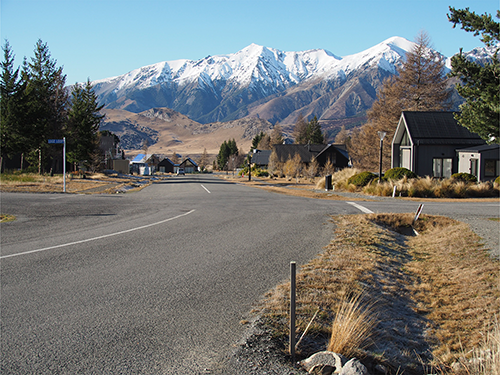 Road weaving through a town between houses with mountains in background