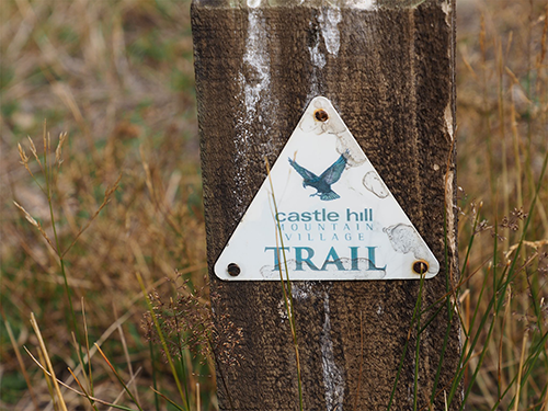Sign which says Castle Hill mountain village trail with trees in background