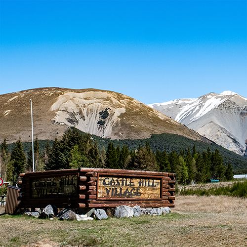 Sign which says Castle Hill Village with mountains in background