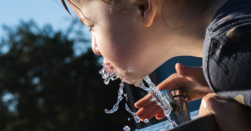 A close up of a child drinking from a water fountain