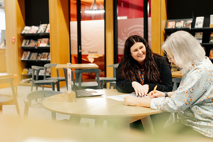Female librarian helping female resident sitting at a table with paperwork