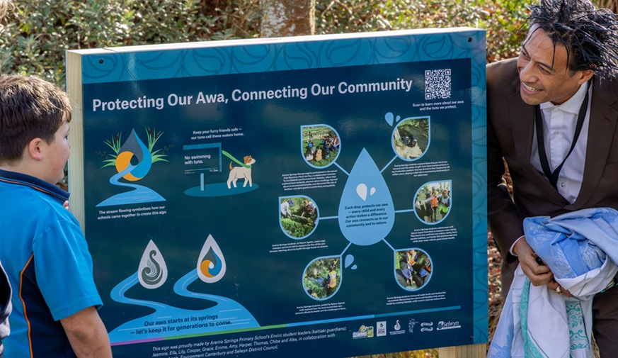 Boy and man unveil a sign about longfin eels installed next to a stream