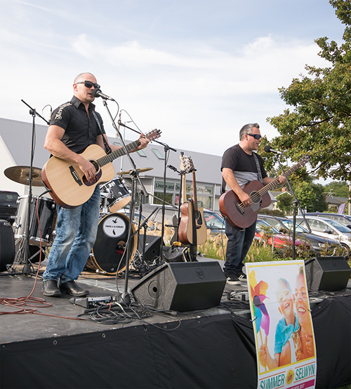 Two men playing guitars on a stage outside