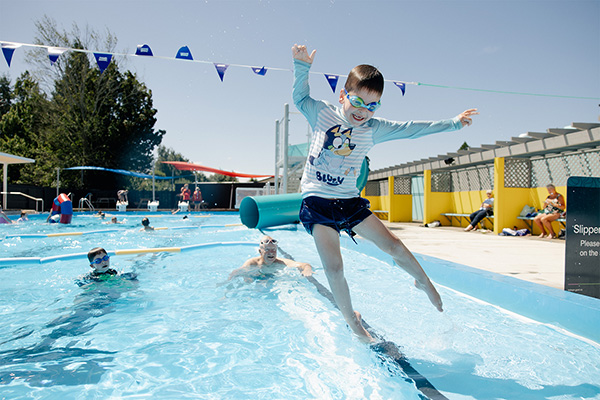 male child jumping in pool with onlookers from a male elderly person and male child