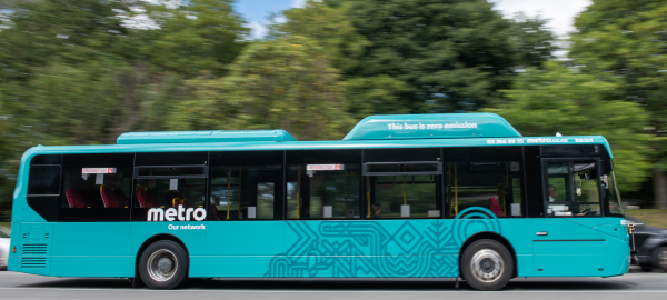 A teal coloured metro bus driving along a tree lined road