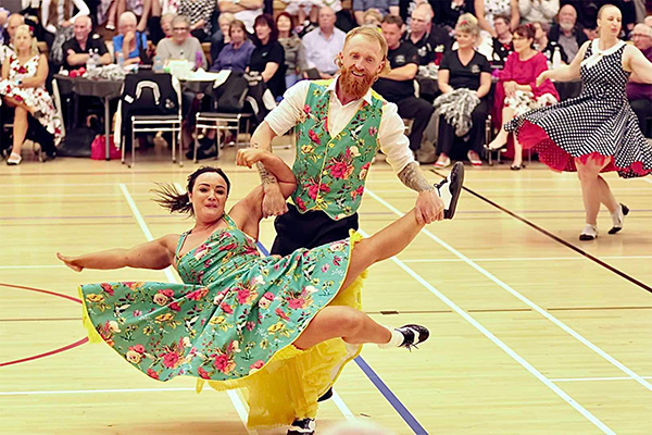 a woman and man dancing to rock'n'roll in green floral attire
