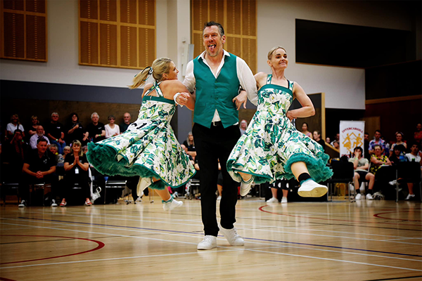 a man in a suit and two women in dresses dancing to rock and roll
