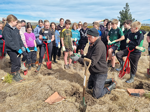 Children gathering around teacher showing how to plant plants