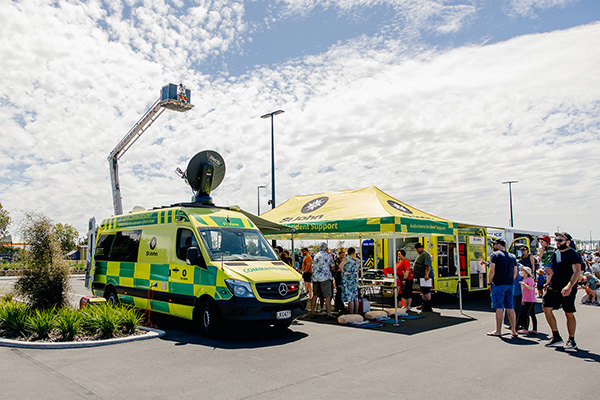 Several people gather outside ambulance and stalls under a blue sky with white clouds