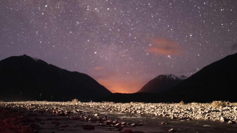 image of stars in a purple sky looking across a river to the mountains in the high country