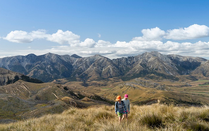 Landscape of mountain scene with two children walking through tussock