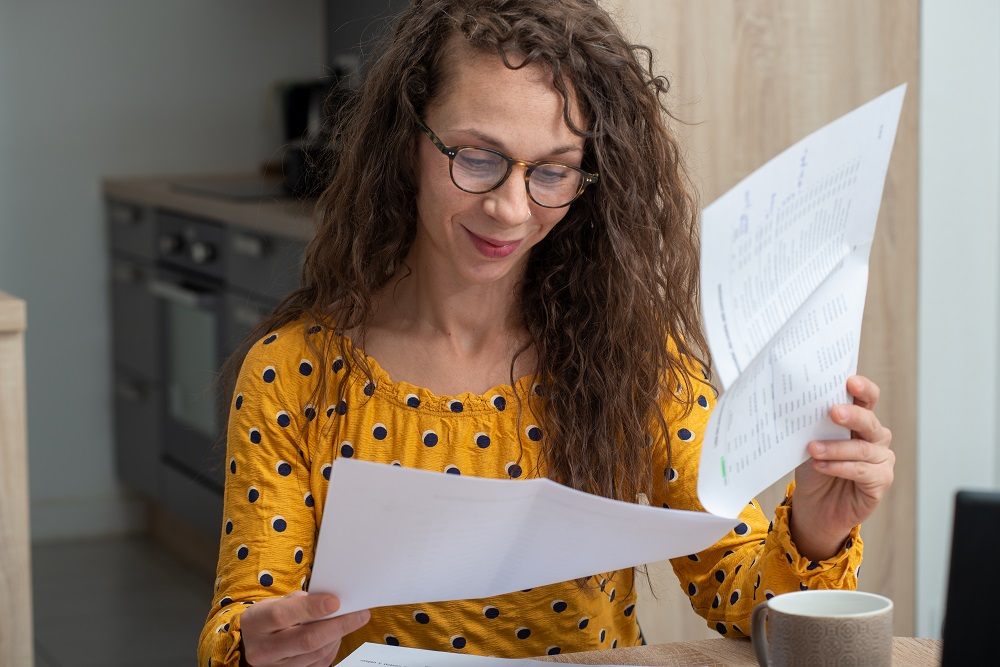 Smiling woman with long curly hair and yellow top with black spots looks through some paperwork