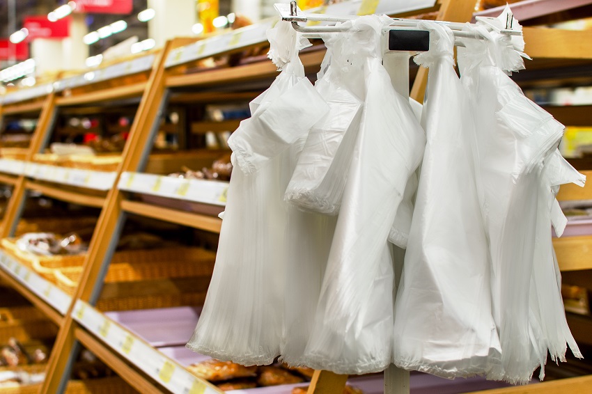 A two piles of white plastic bags hang vertically off a metal hook in front of some wooden shelves