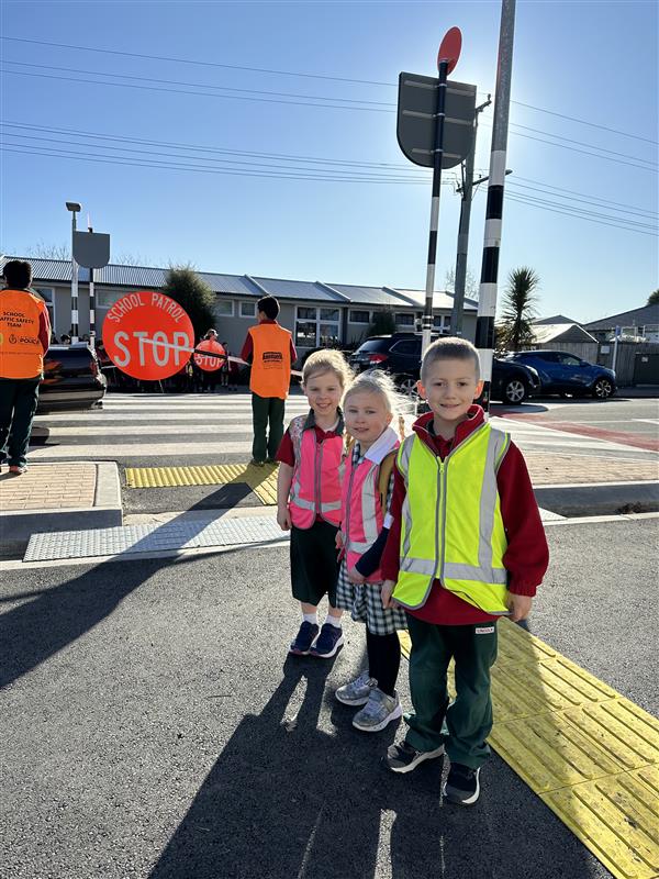 Maddie, Sophie and Frank, aged five, wearing high vis vests standing next to the new crossing at Lincoln Primary School