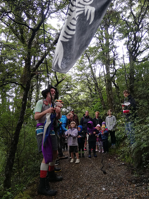 A pirate with a flag leads several children into a forest