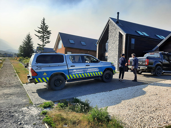 Vehicle parked outside houses with man and women standing outside