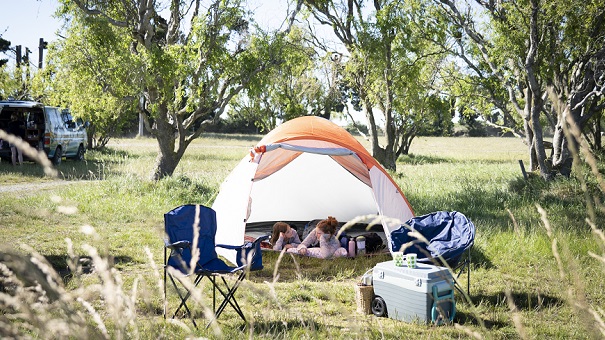 an open tent in a campground with two women lying inside talking