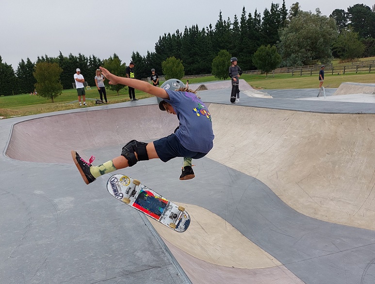 A young skater in the air with his board underneath him as he comes up out of the skate bowl