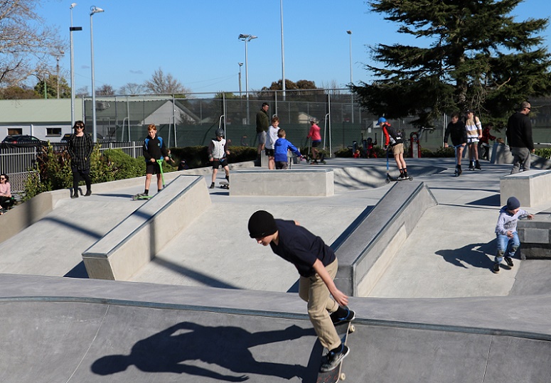 A skater coming down into the intermediate bowl with skaters and scooters using ramps behind