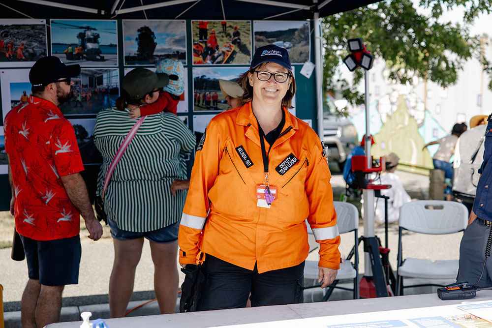 A smiling volunteer in uniform behind a low table in a gazebo