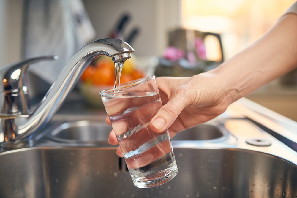 A persons hand holding an almost full glass under a running sink tap