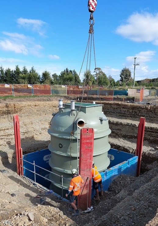 Men in high visibility monitor a grey tank being lowered into a hole by a crane